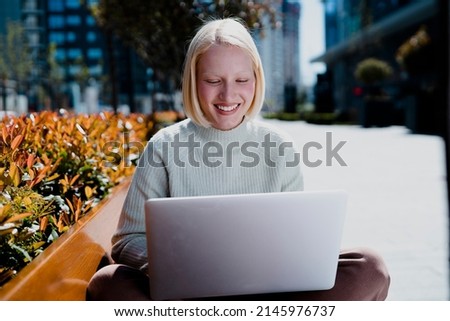 Happy young girl sitting in the park using laptop. Beautiful woman having video call.