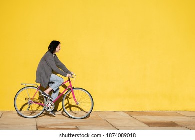 happy young girl smiles as she rides her retro pink bike along a colorful yellow wall, concept of active lifestyle and sustainable mobility, copy space for text
