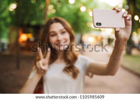 Happy young girl taking a selfie while standing at the park