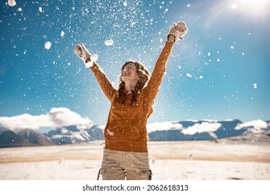 Happy Young Girl Is Tossing The Snow In Mountains. Winter Vacations Concept