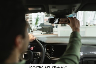 Happy young guy sitting in new car, adjusting rear view mirror, checking modern auto before purchase at dealership centre. Millennial man test driving automobile, selecting vehicle at showroom store - Powered by Shutterstock