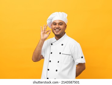 Feliz joven y guapo chef asiático con uniforme y puesto de pie, buen gusto delicioso gesto de mano delicioso. Cocinando al hombre indio El chef de la ocupación o la panadería People en el restaurante y el hotel de la cocina.