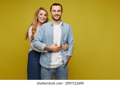 Happy Young Heterosexual Couple Hugging And Showing Happiness On The Yellow Background. A Young Man And Adorable Woman Wearing Casual Clothes Posing Over Yellow Background