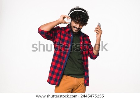 Happy young Hindi man listening to the music in headphones isolated over white background. Indian fan enjoying podcast radio favorite song band in mobile application online