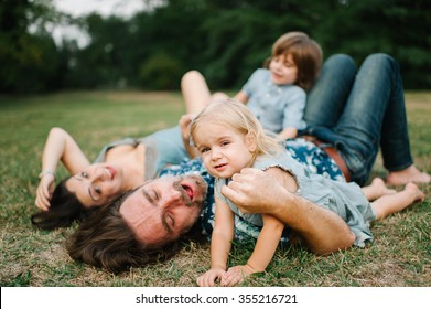 Happy Young Hipster Family Having Fun, Bowl,  Rising Up, Piggyback Ride Their Children In Park On Summer Sunset