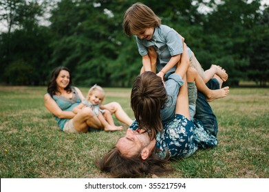 Happy Young Hipster Family Having Fun, Bowl,  Rising Up, Piggyback Ride Their Children In Park On Summer Sunset 
