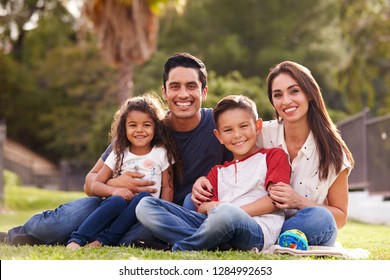 Happy young Hispanic family sitting the on grass in the park smiling to camera, close up