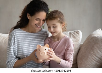 Happy Young Hispanic Mom And Small Teen Daughter Feel Provident Economical Make Investment. Smiling Latino Mother And Girl Child Save Money Cash In Piggybank. Banking, Financial Stability Concept.