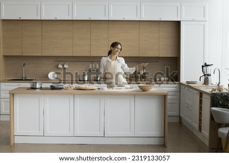 Happy young housewife in apron dance while cook pizza in cozy kitchen, listen to favourite music, looks carefree enjoy household chores on pastime alone at home, preparing homemade food, relish hobby