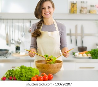 Happy young housewife mixing vegetable salad