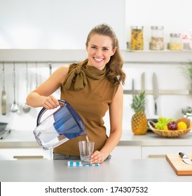 Happy Young Housewife Pouring Water Into Glass From Water Filter Pitcher