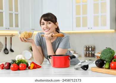 Happy young housewife with spoon and raw pasta at white marble table in kitchen. Cooking process - Powered by Shutterstock