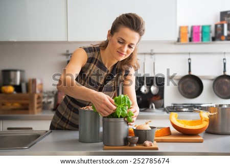 Happy young housewife using fresh basil while cooking in kitchen