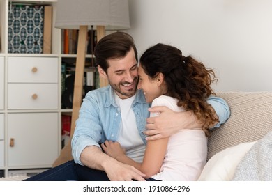 Happy young husband and wife hug on sofa spend time in warm embraces of one another share lovers secrets confessions. Excited newlyweds buying house first time cuddle on couch enjoy new family home - Powered by Shutterstock