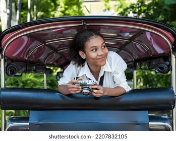 Happy young independent traveller girl holding camera and sitting in back seat TUK TUK driver exploring Chiang Mai, Thailand , cheerful woman taking tuktuk travel in Thailand during summer vacation