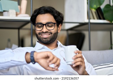 Happy young indian business man drinking coffee in morning checking time looking at wrist watch starting day or finished work on friday fast well done sitting in office. Effective time management - Powered by Shutterstock