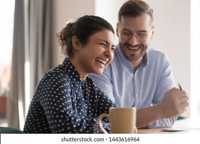 Happy young indian business woman laughing at funny joke with friendly colleague in office, cheerful diverse multi ethnic coworkers team having fun talking working together at break sit at desk - Powered by Shutterstock