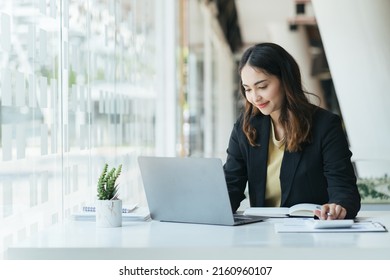 Happy Young Indian Business Woman Entrepreneur Using Computer Looking At Screen Working In Internet Sit At Office Desk, Smiling Hindu Female Professional Employee Typing Email On Laptop At Workplace