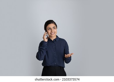Happy young Indian businesswoman talking on mobile phone, looking away, standing by white background. mixed race millennial girl speaking having telephone call, speaking, smiling. Isolated portrait