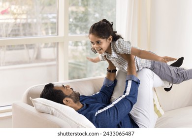 Happy young Indian dad lying on back, holding little daughter girl on arms and legs, lifting child up in air for playing airplane, laughing, having fun, enjoying leisure, fatherhood, doing acroyoga - Powered by Shutterstock