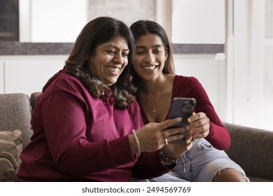 Happy young Indian daughter woman showing application on smartphone to cheerful mature mom. Mother and adult kid using mobile phone for Internet communication, laughing, having fun - Powered by Shutterstock