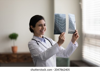 Happy young Indian doctor looking at xray radiography images. Physician, surgeon reviewing scan of patient bones, smiling at good screening test result. Medical checkup, healthcare, radiology concept