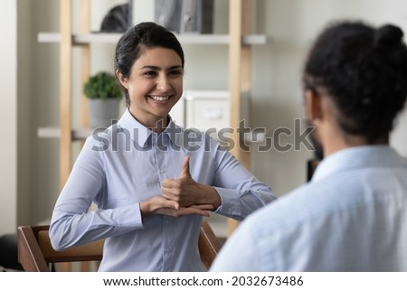 Happy young indian ethnic woman making gestures, practicing sign language with african american friend or therapist, diverse millennial people communicating, enjoying pleasant conversation indoors.