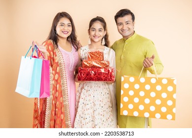 Happy Young Indian Family Holding Gift Box And Shopping Bags Celebrating Diwali Festival Together Isolated On Studio Background. Festive Shopping And Sale, Looking At Camera.