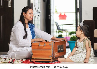 Happy Young Indian Female Music  Teacher Teaching Kid How To Sing While Playing Harmonium Instrument,  Hobby Classes. Mother Daughter Relationship And Activity.