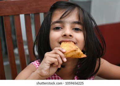 Happy Young Indian Girl Child Eating Her Samosa, Sambusa In Mumbai, India.