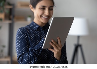Happy young Indian girl using online ecommerce app on tablet computer, shopping on internet, making quick payment. Millennial woman reading ebook on digital device, touching screen, smiling