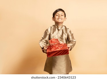 Happy young indian kid boy wearing traditional kurta outfit holding red gift boxes celebrating of diwali festival isolated on beige background. Child holding present. - Powered by Shutterstock