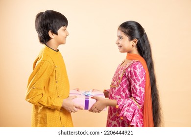 Happy young indian kids exchange gift box celebrating diwali festival together isolated on studio background. brother give present to sister. - Shutterstock ID 2206444921