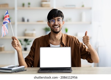 Happy Young Indian Man English Teacher Showing Flag Of UK And Thumb Up, Sitting In Front Of Laptop At Office, Teaching Via Online Courses, Leading Language School, Copy Space. Online Education Concept