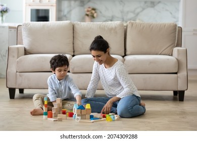 Happy young Indian mom helping preschool son to build toy towers from wooden construction blocks, playing with kid on heating floor at home. Babysitter watching child. Motherhood, daycare concept - Powered by Shutterstock