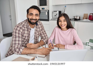 Happy Young Indian Parent Father Helping Teenage Child Daughter Distance Learning Online Together At Home. Teen School Kid Girl Studying In Kitchen With Dad Looking At Camera Sitting At Kitchen Table.