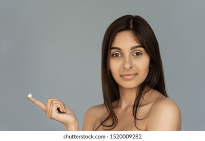 Happy Young Indian Woman Beautiful Face Hold Cream On Finger Look At Camera Isolated On Grey Studio Background, Pretty Healthy Girl Model Advertise Facial Skin Care, Natural Beauty Concept, Portrait