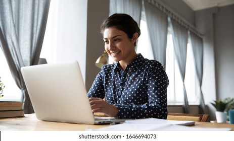 Happy young Indian woman sit at desk in living room browsing Internet working on computer gadget, smiling millennial ethnic girl studying online on laptop, take course or training, education concept - Shutterstock ID 1646694073
