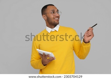 Happy young intern holding notebook and pen on light grey background