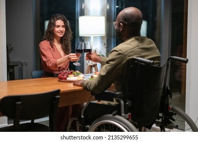 Happy young interracial couple sitting by festive table and toasting with red wine during romantic dinner at home or restaurant - Powered by Shutterstock