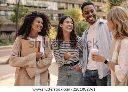 Happy young interracial students chatting with each other after class standing outside. Guy and girls wear casual clothes to study. Lifestyle concept, sincere emotions