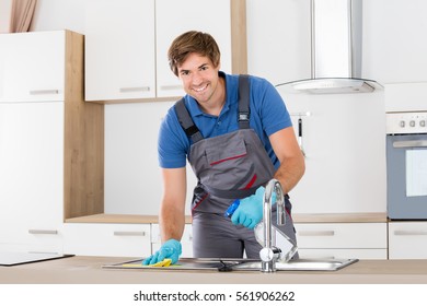 Happy Young Janitor Cleaning Kitchen Sink With Spray And Sponge