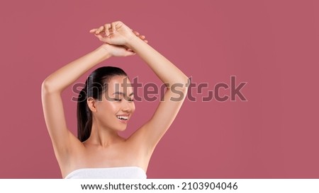 Happy young japanese woman wrapped in white towel raising hands up and smiling, showing her clean and hairless armpits, posing over purple studio background, panorama with copy space