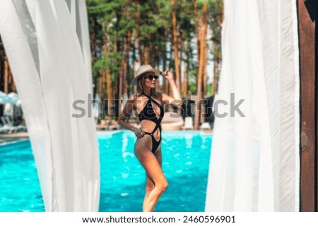 Happy young lady in black swimsuit and sunglasses posing near swimming pool outdoors. Copy space. Summer, vacation and lifestyle concept