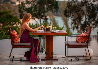 Happy Young Lady Eating Delicious Food In Fine Dining Outdoor Restaurant. Sexy Girl In Elegant Evening Dress On Date. Romantic Dinner On Sunset. Concept Of Proposal Or Honeymoon