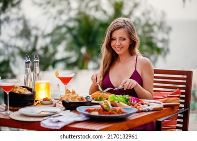 Happy Young Lady Eating Delicious Food In Fine Dining Outdoor Restaurant. Sexy Girl In Elegant Evening Dress On Date. Romantic Dinner On Sunset. Concept Of Proposal Or Honeymoon