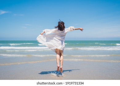 Happy Young Lady Are Jumping, Feel Relax, Fun, And Enjoy Holiday At Tropical Coast Beach With Clear Cloud And Blue Sky Background