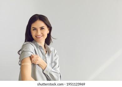 Happy young lady on gray empty blank text copyspace studio background looking at camera, smiling and showing arm after vaccine injection. Coronavirus, Covid-19, flu vaccination and immunization - Powered by Shutterstock