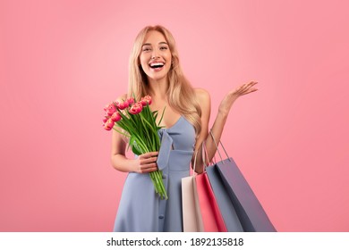 Happy Young Lady With Shopping Bags And Bouquet Of Tulips Buying Gifts For Spring Holiday Over Pink Studio Background. Woman's Day Sale, Discount Or Promotion Concept