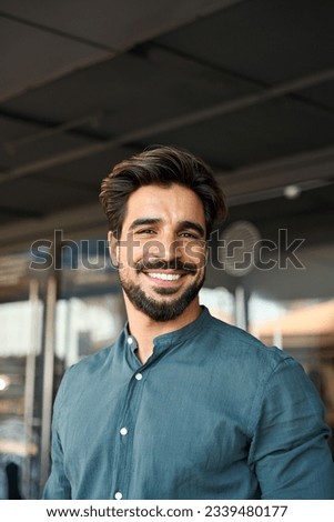 Happy young Latin business man looking at camera, vertical portrait. Smiling bearded businessman, handsome male entrepreneur, professional employee looking at camera standing outside office.